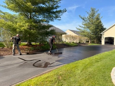 Two men are painting a driveway in front of a house.