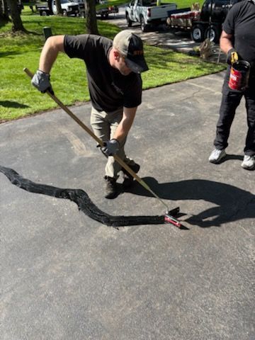 A man is using a broom to spread asphalt on a driveway.
