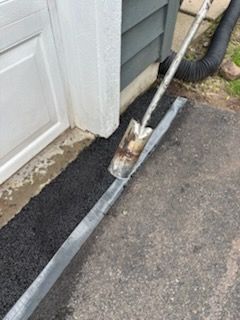 A shovel is being used to spread asphalt on the sidewalk next to a garage door.