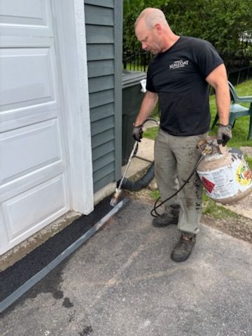 A man is standing next to a garage door holding a propane tank.