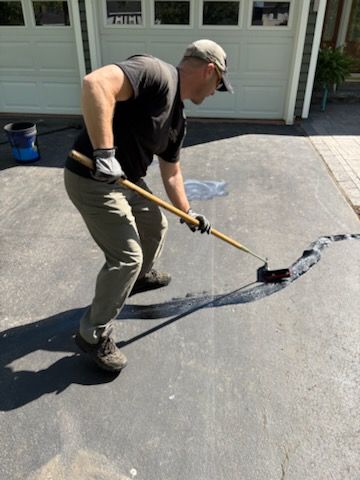 A man is painting a driveway with a roller.