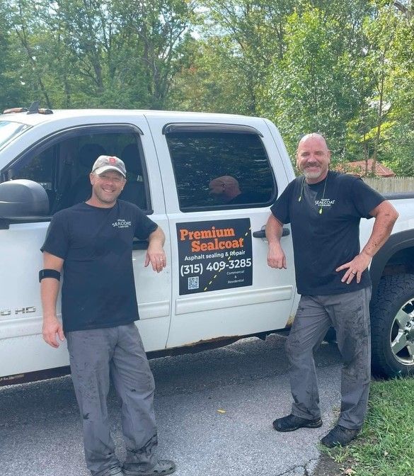 Two men standing in front of a truck that says premium sealcoat