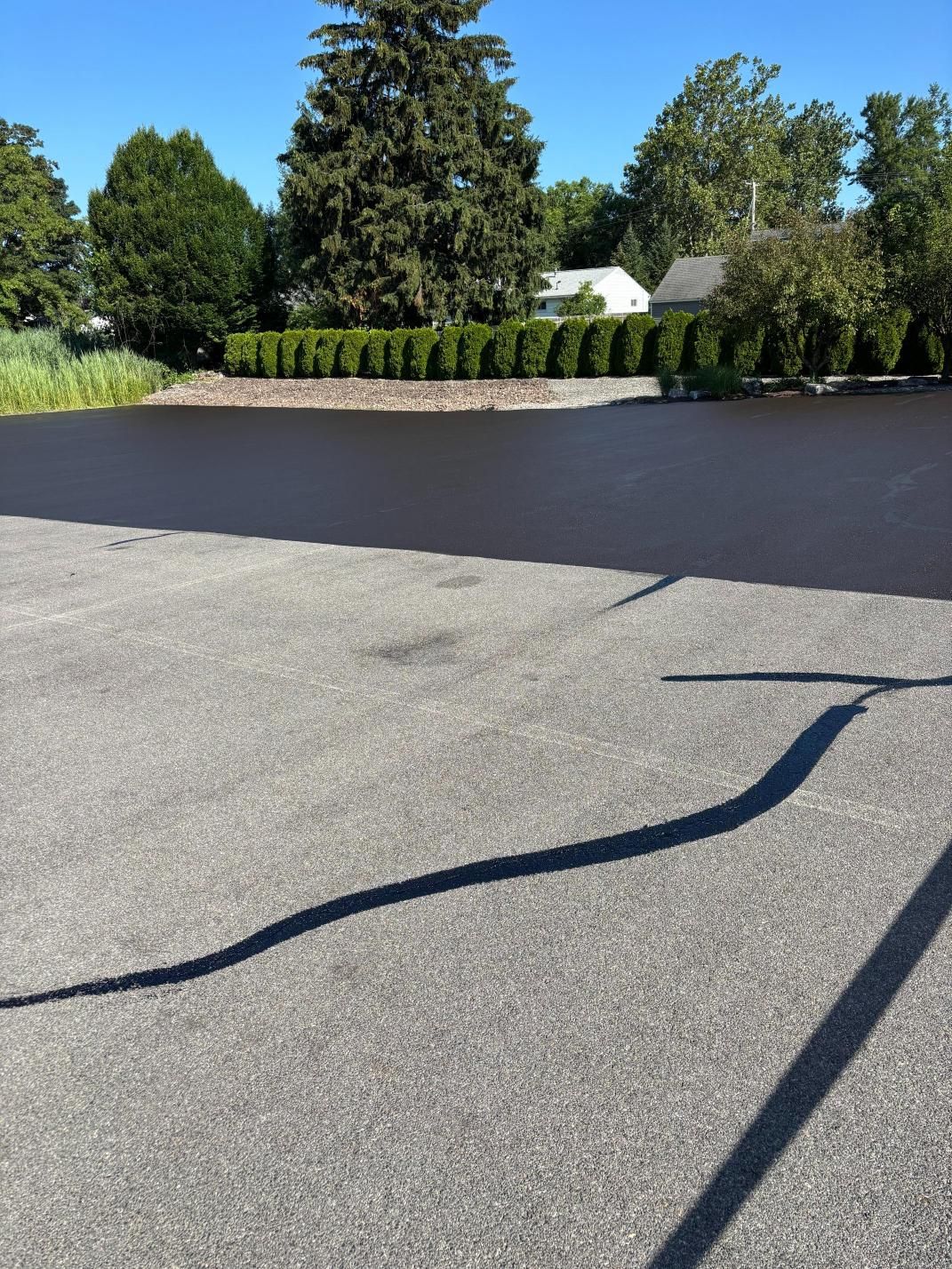 A shadow of a car is cast on the asphalt of a driveway
