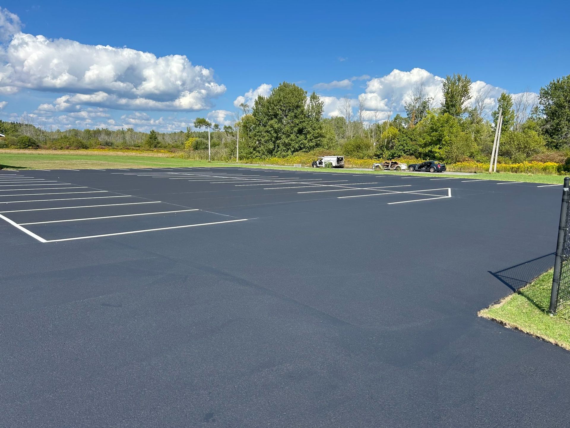 Newly paved parking lot with white parking space lines, blue sky with clouds in the background.