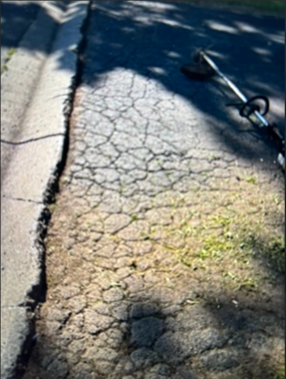 A cracked sidewalk with a shadow of a lawn mower on it