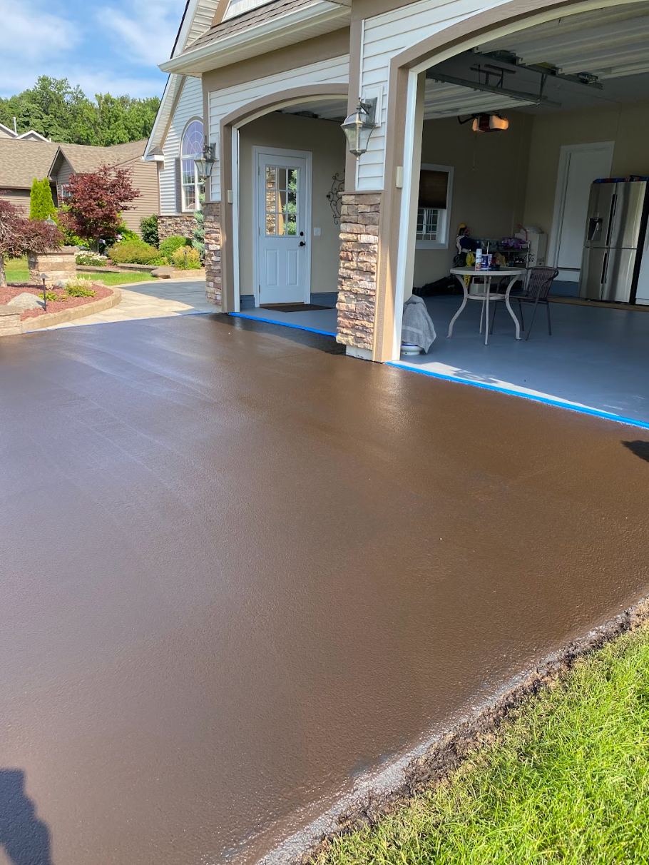 A concrete driveway is being painted brown in front of a house.