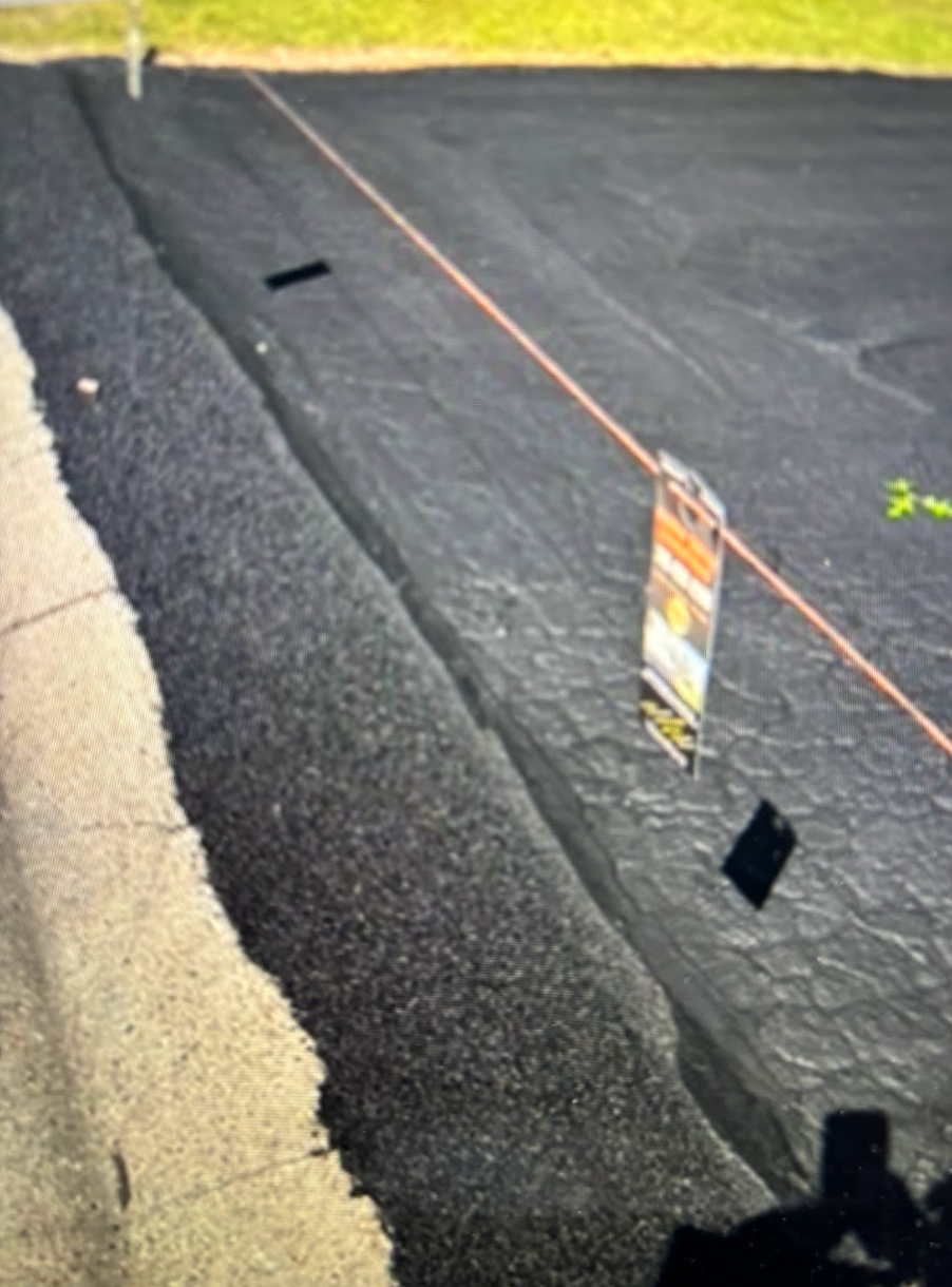 A shadow of a person is reflected in a sign on the side of a road.