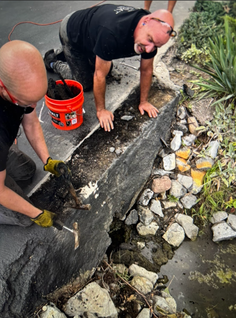 Two men are working on a sidewalk next to an orange bucket
