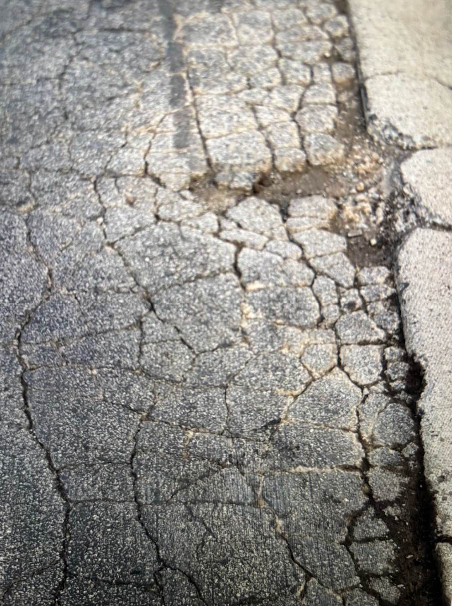 A close up of a cracked asphalt road next to a sidewalk.