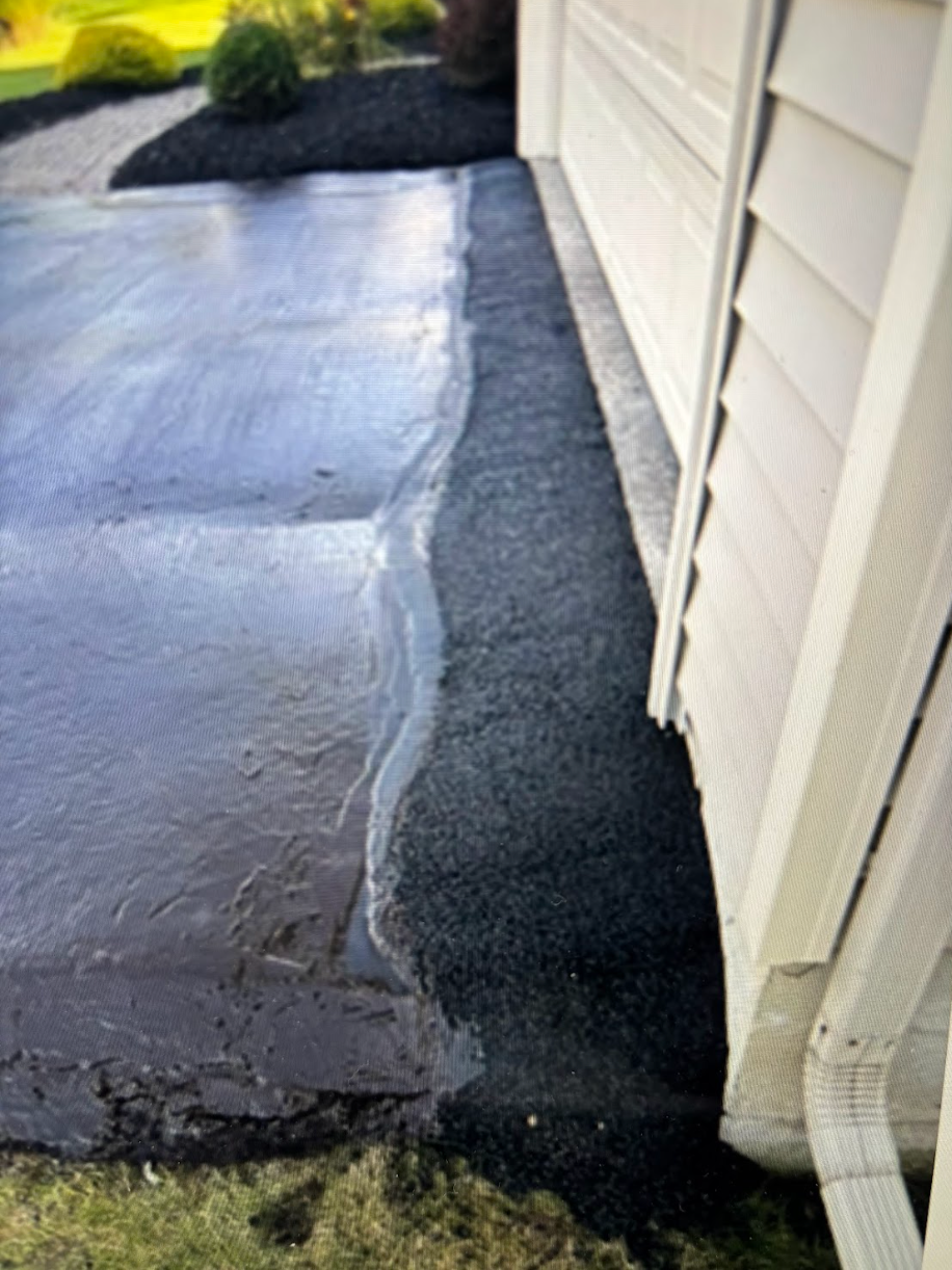 A black concrete driveway next to a white house.