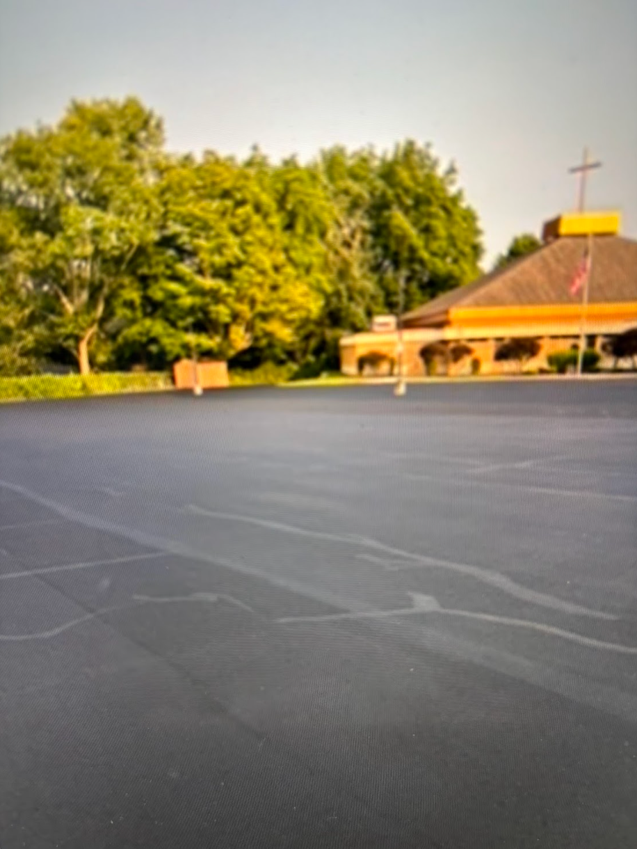 A parking lot with a building in the background and trees in the foreground.