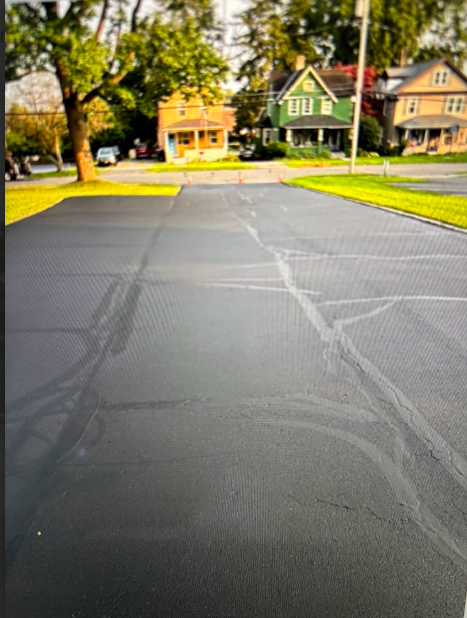 A basketball court in a residential neighborhood with a green house in the background.