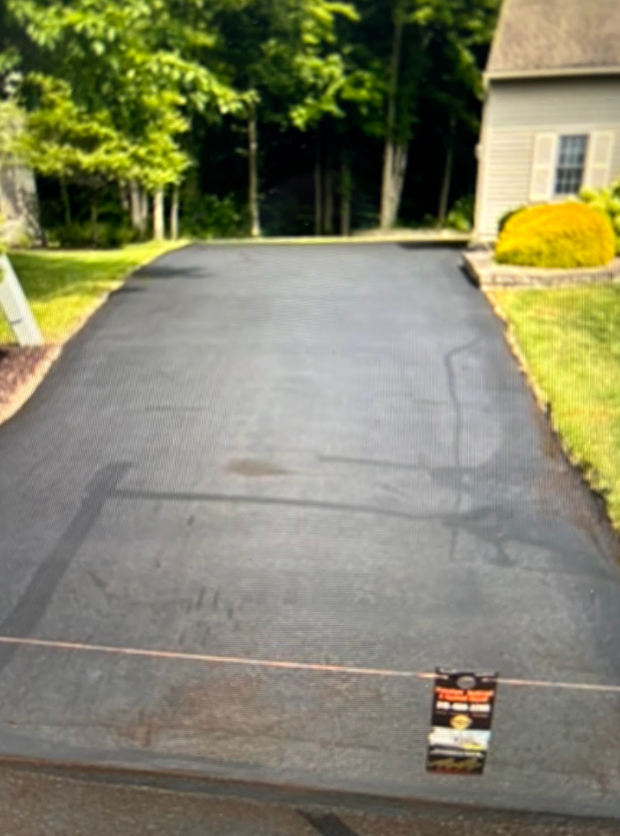 A black asphalt driveway with a house in the background