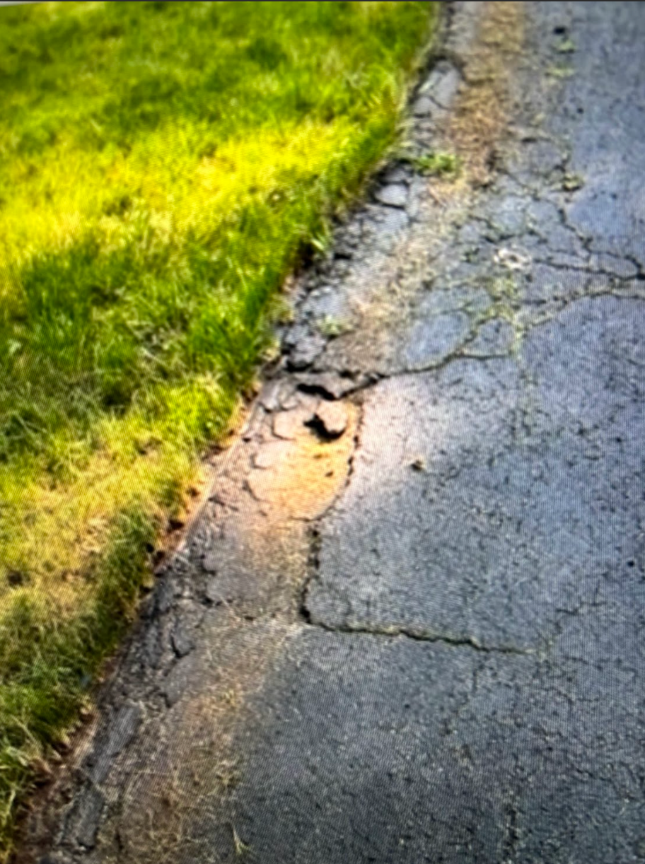 A close up of a cracked asphalt road next to a grassy area.