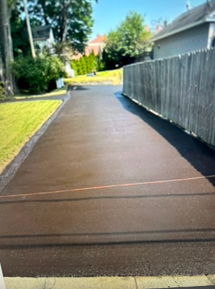 A driveway with a wooden fence and a house in the background.