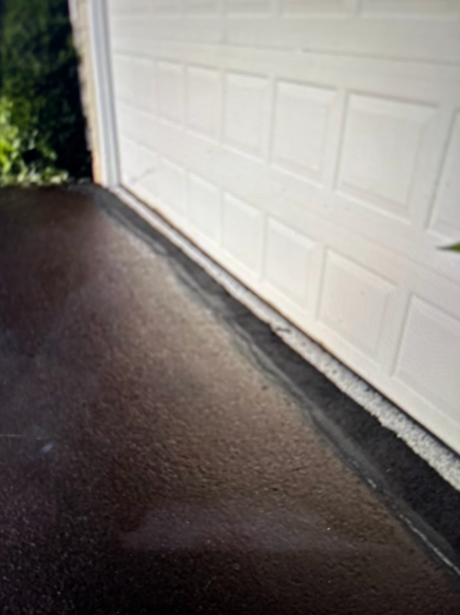 A white garage door is sitting next to a black asphalt driveway.