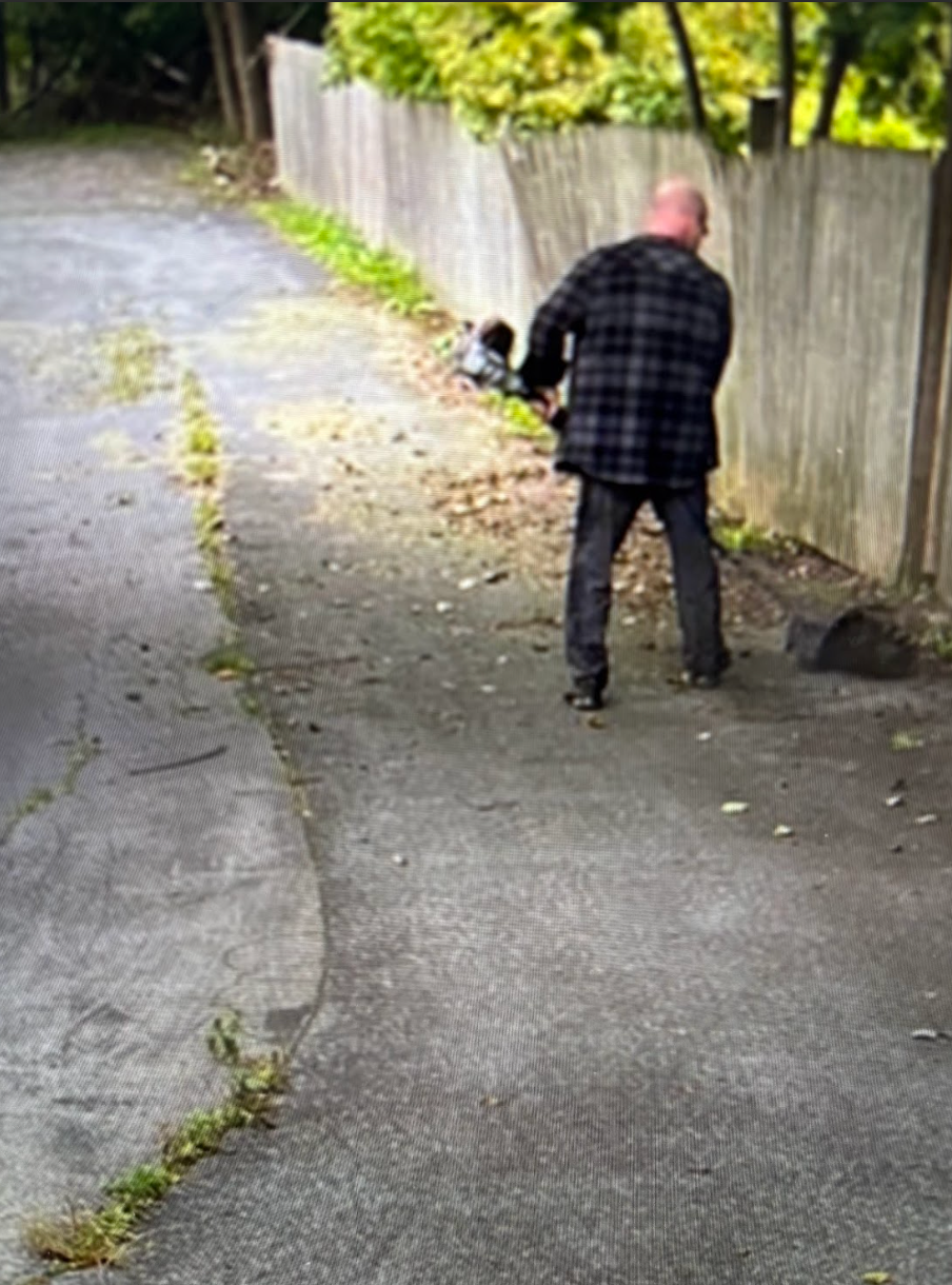 A man is walking down a sidewalk next to a fence.