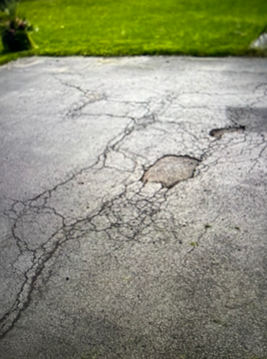 A cracked asphalt driveway with a patch of grass in the background.