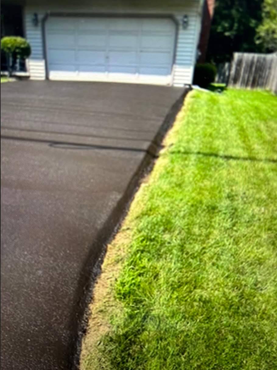 A driveway with a lot of grass and a garage in the background.