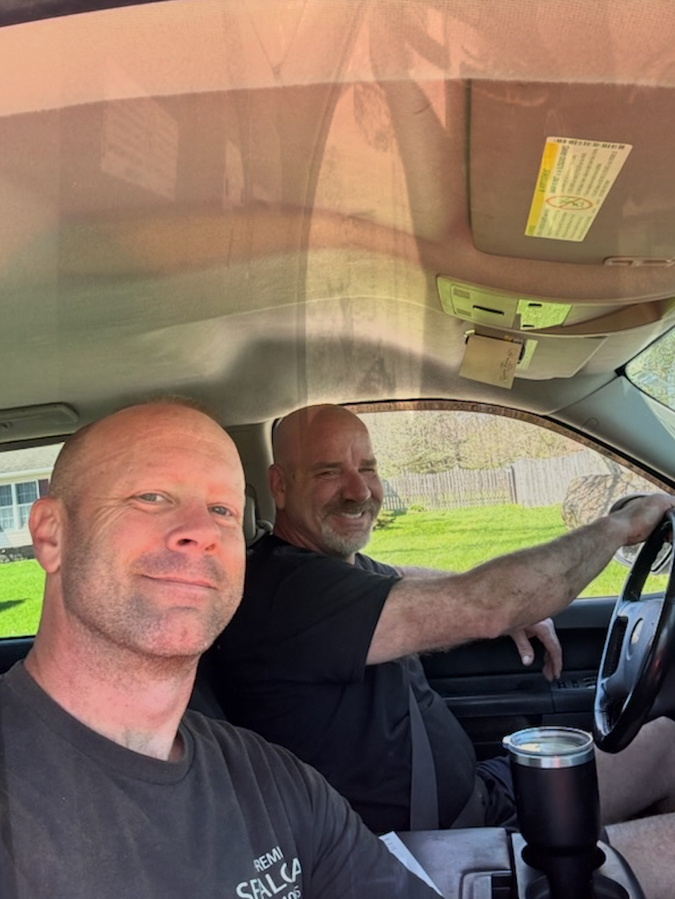 Two men are sitting in a car and smiling for the camera.