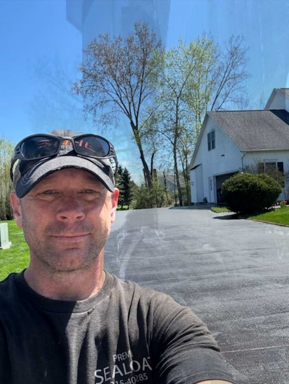 A man wearing sunglasses and a hat is taking a selfie in front of a house.