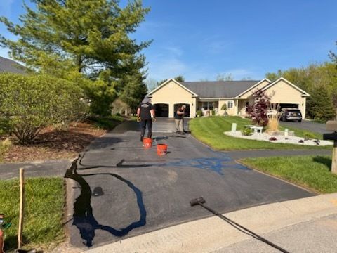 A man is painting a driveway in front of a house.