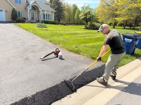 A man is spreading asphalt on the sidewalk in front of a house.
