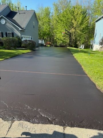 A driveway with a house in the background and trees on the side.