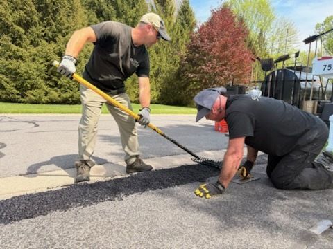 Two men are laying asphalt on the side of a road.