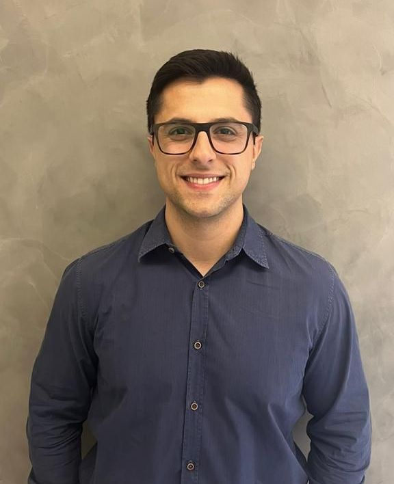 Um homem de óculos e camisa azul está sorrindo para a câmera.