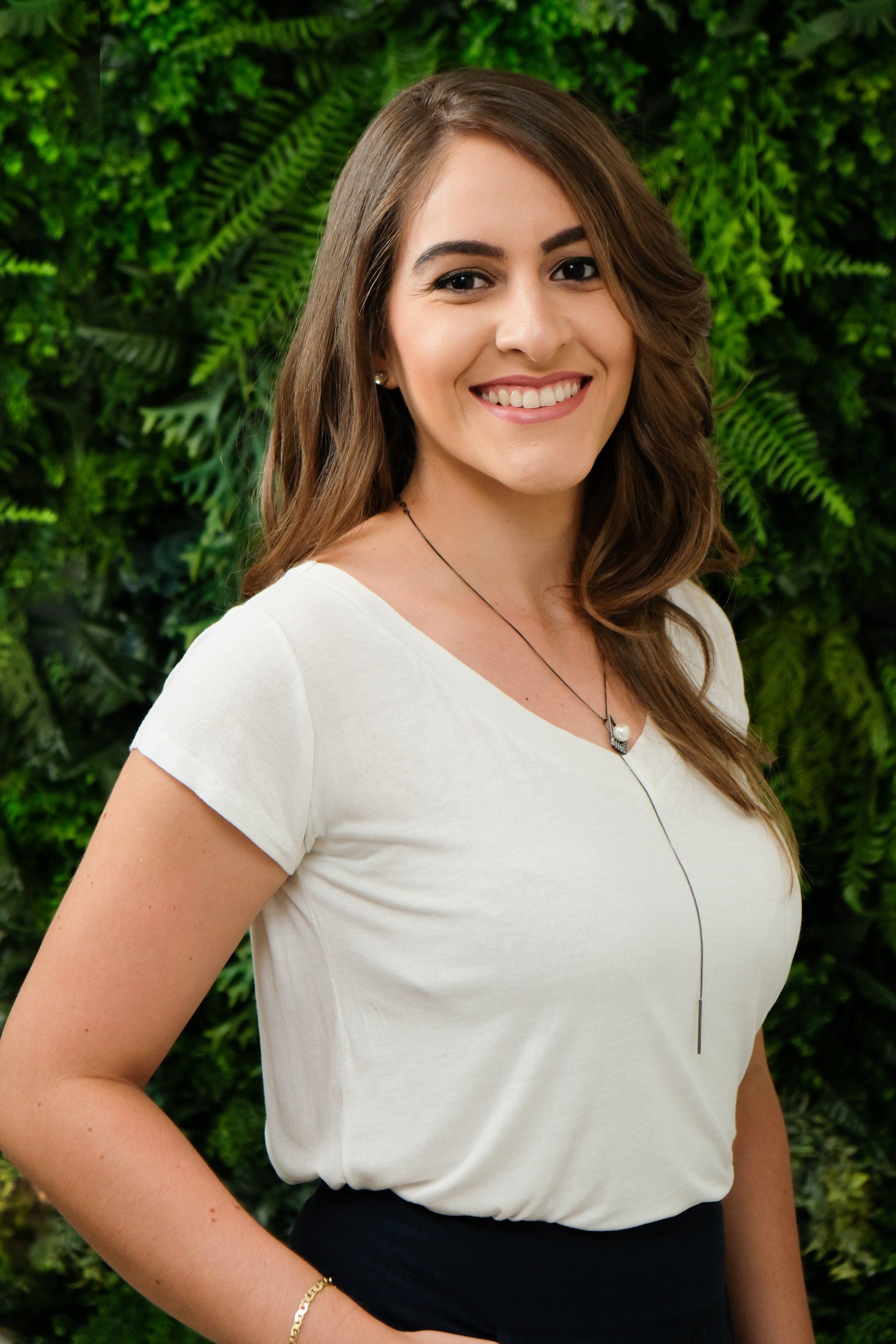 Uma mulher de camisa branca e saia preta está sorrindo em frente a uma parede verde.