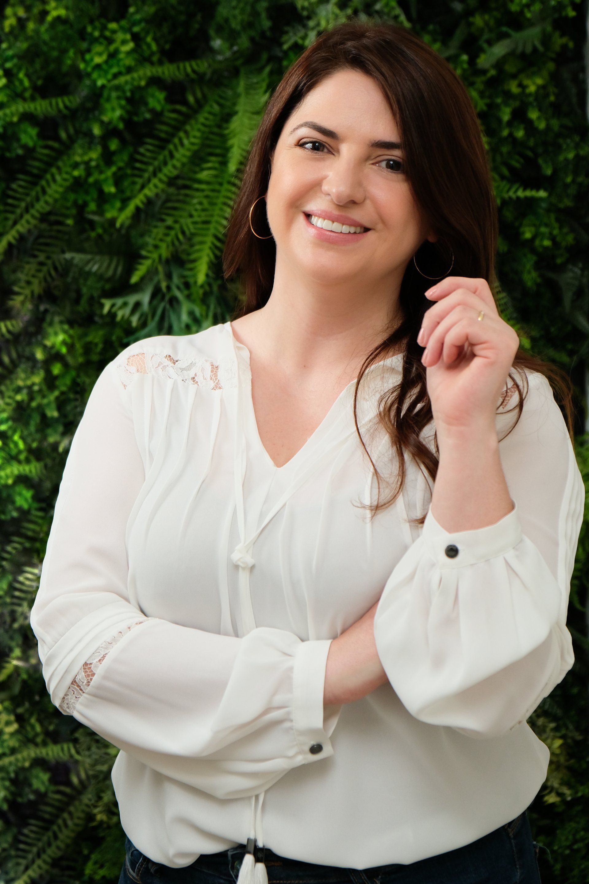 Uma mulher de blusa branca está parada em frente a uma parede verde.