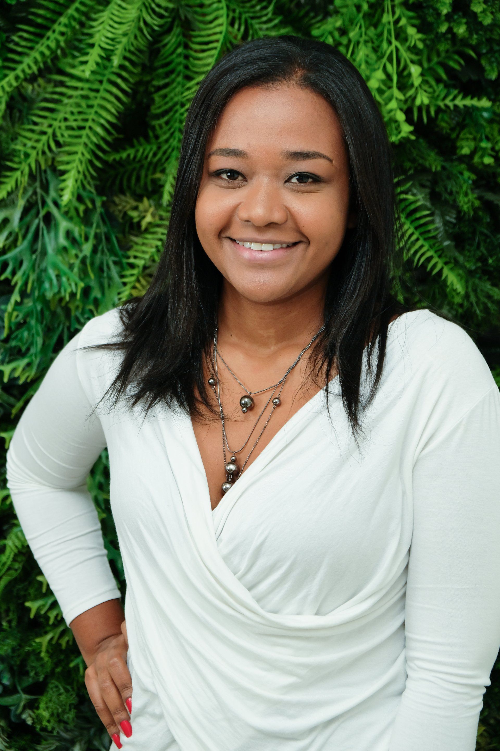 Uma mulher de camisa branca está sorrindo na frente de um arbusto de samambaia.