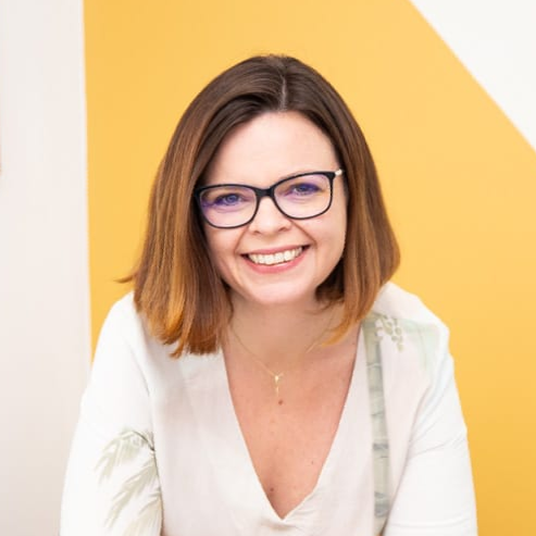 Uma mulher de óculos e camisa branca está sorrindo.