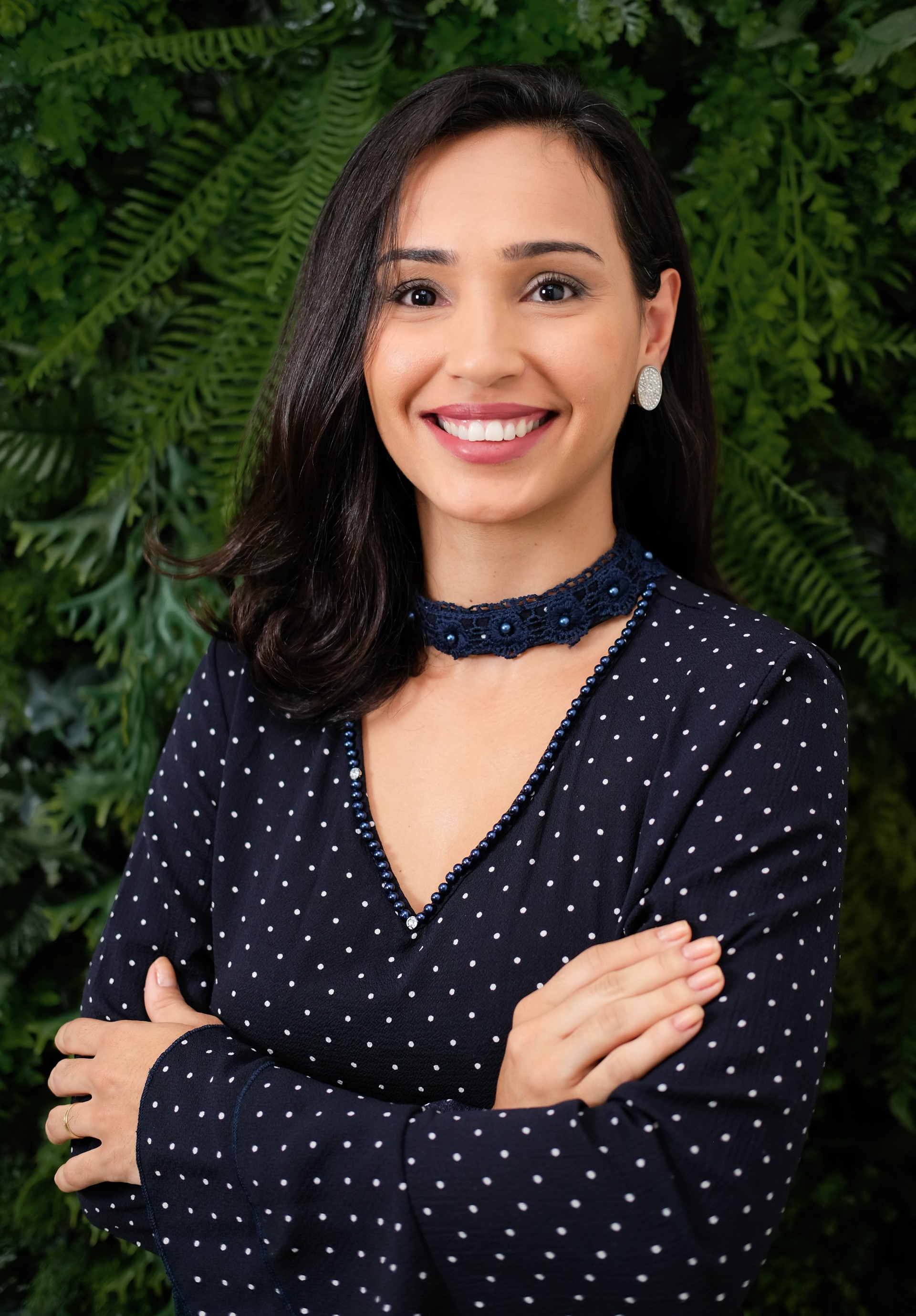 Uma mulher com um vestido de bolinhas está sorrindo com os braços cruzados.