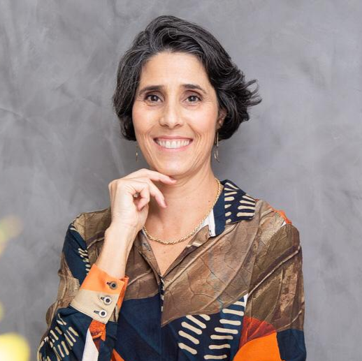 Uma mulher com uma camisa colorida está sorrindo com a mão no queixo.