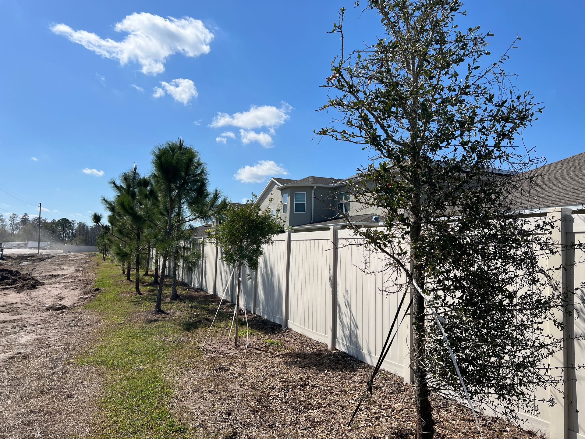 a white fence with trees in front of it and a house in the background .