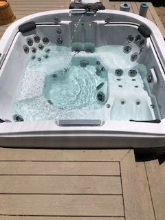 Hot tub filled with water on a wooden deck. Jets are on, creating bubbles.