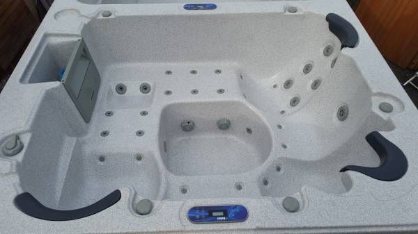 White hot tub with multiple jets, seating areas, and blue control panel.