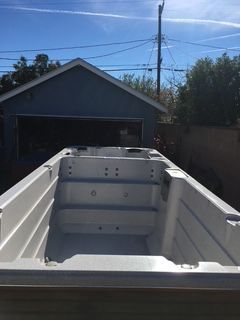Empty rectangular white swim spa in a backyard, blue garage in the background on a sunny day.