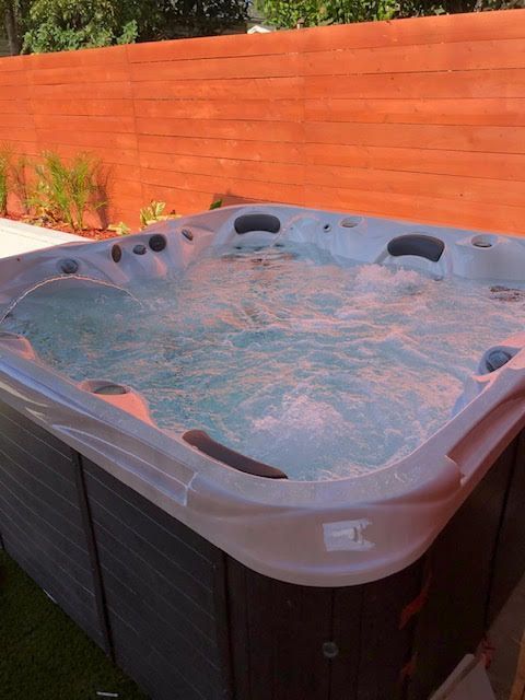Hot tub filled with water, surrounded by a wood enclosure and a red fence.
