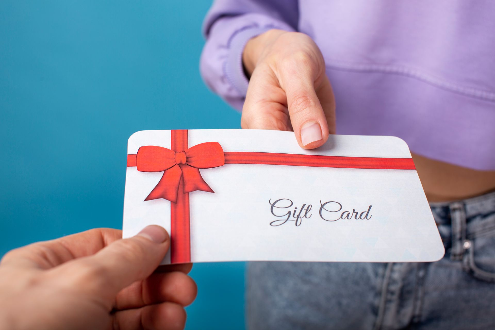 Person handing a white gift card with a red bow to another person.