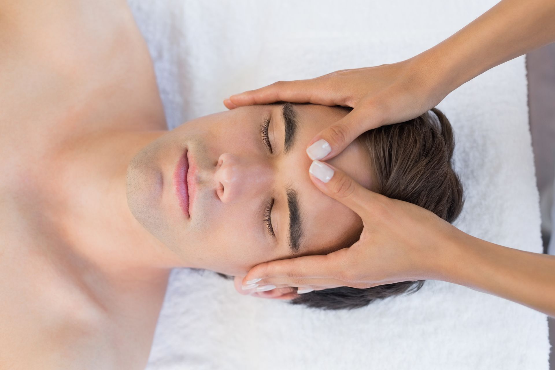 Person receiving a head massage on a massage table. Hands on forehead, eyes closed.