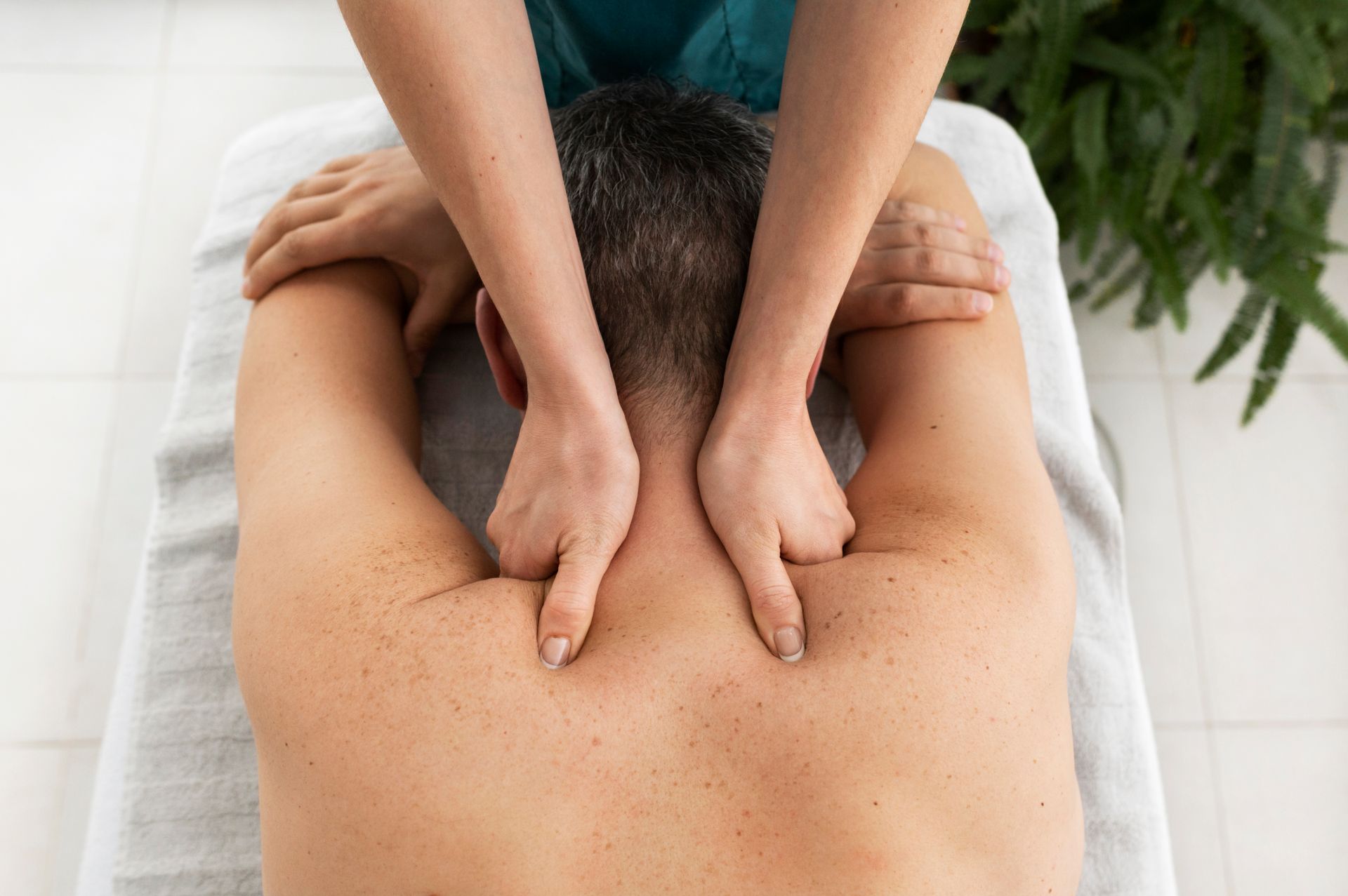 Hands massaging a person's upper back and neck on a massage table.