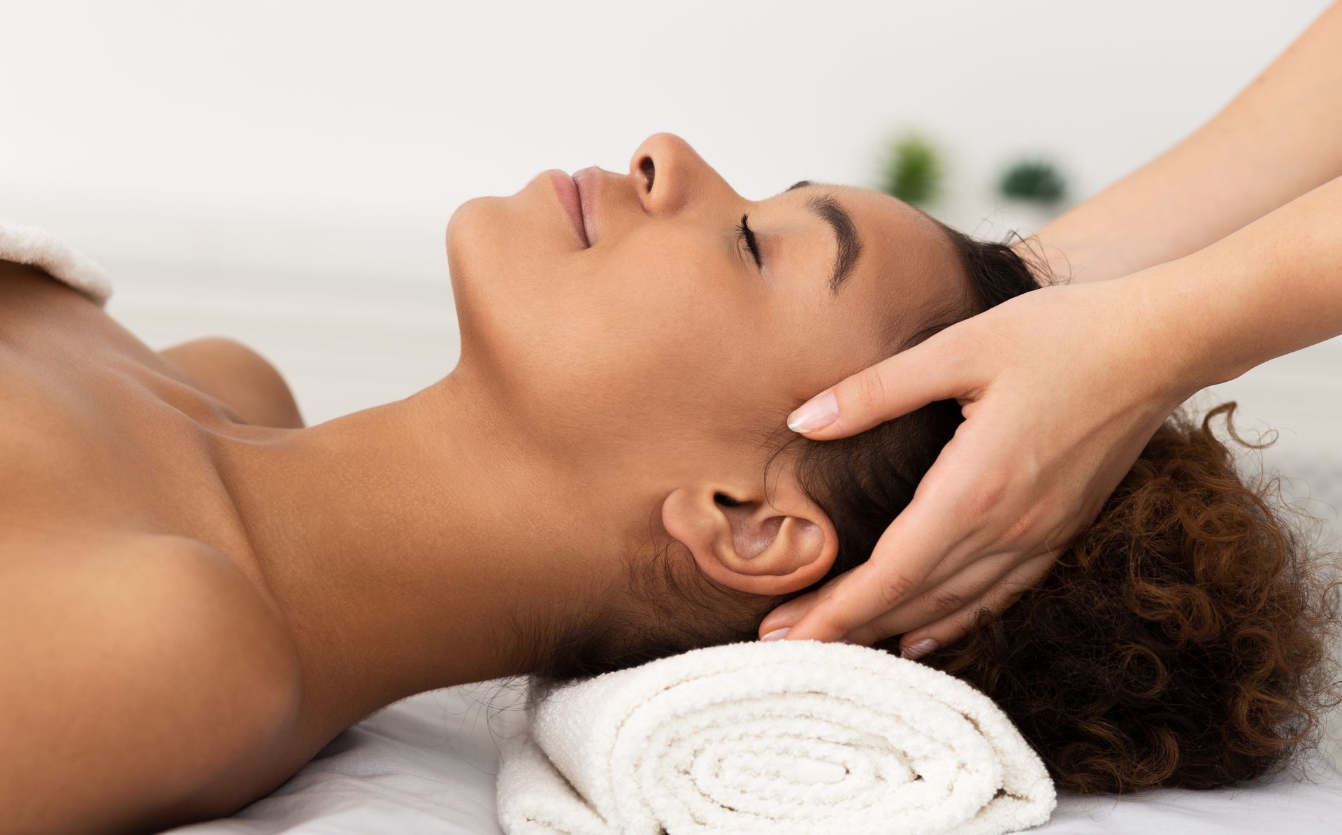 Woman receiving a head massage; resting on a white towel, eyes closed.