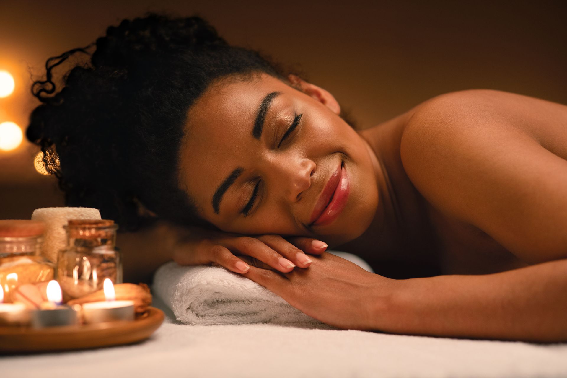 Woman smiles, eyes closed, receiving a massage on a table lit by candles.