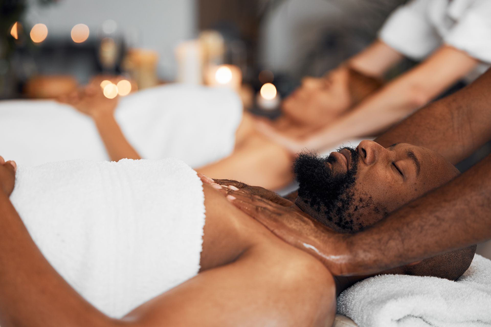 People receiving massages at a spa; two individuals lying face up while masseuses work on their chests and shoulders.