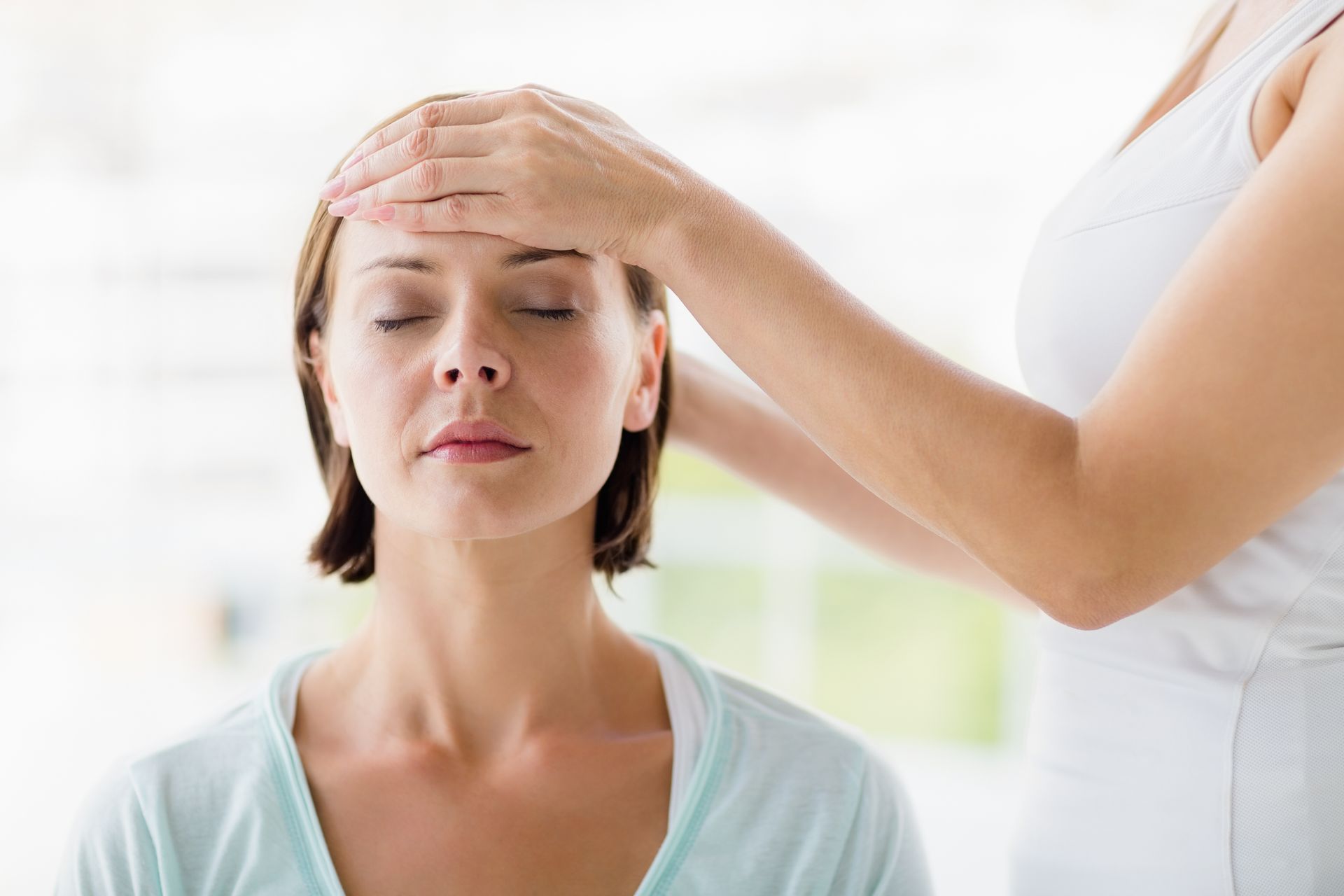 Woman receives a forehead massage from another person in a bright room