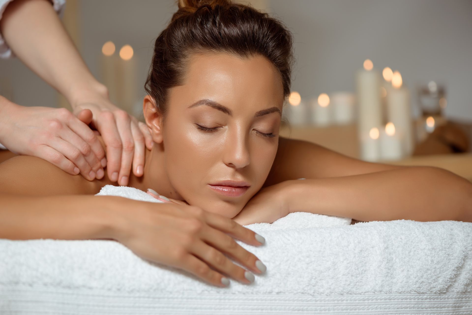 Woman receiving a back massage, relaxing on a towel with candles in the background.