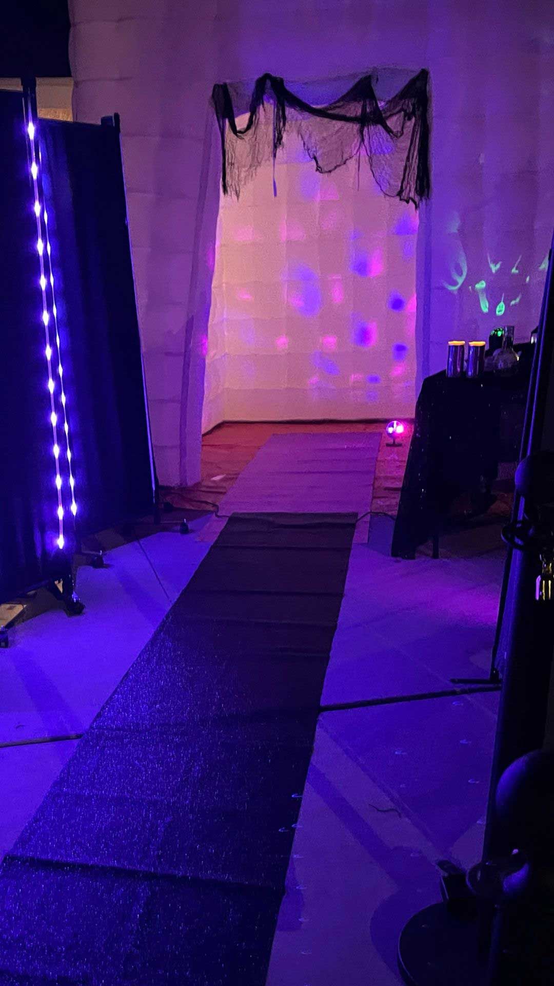 A hallway with purple lights on the walls and a black rug on the floor.